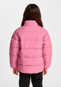 Rosa vadderad jacka med en upprätt krage, försedd med quiltade sektioner och elastiska muddar. Den svarta fodringen kontrasterar mot ytterfärgen.