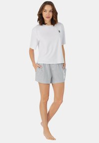 Weißes kurzärmliges T-Shirt mit einem kleinen Logo, kombiniert mit hellgrauen Shorts mit einer Frontknopfverschlus und einem auffälligen Druckdesign.