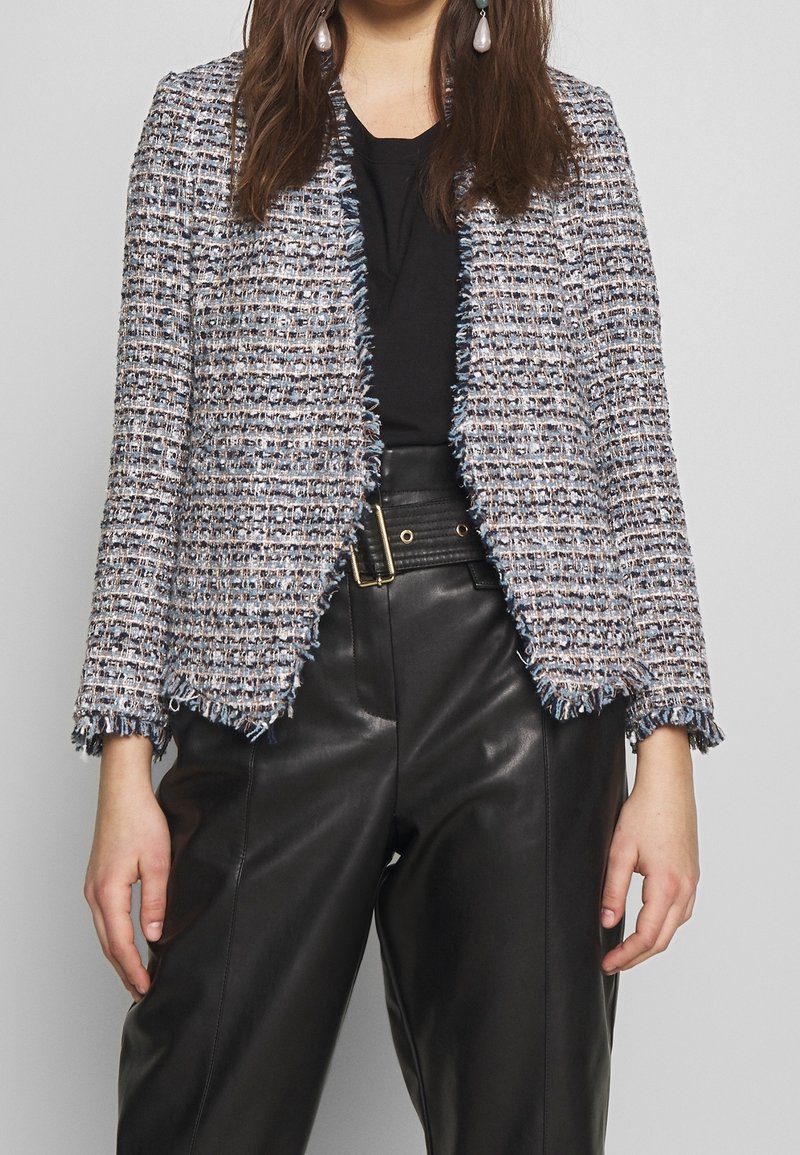 Texturovaná tweedová bunda v odstínech modré a šedé. Design s otevřeným předním dílem a třepenými okraji. Doplněná o černé kožené kalhoty s vysokým pasem.