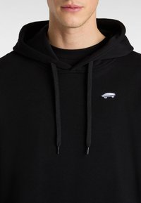 Felpa nera con cappuccio realizzata in tessuto morbido, con tasca a marsupio e cordini regolabili. Presenta un piccolo logo bianco a forma di skateboard sul petto.