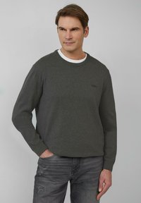 Donkergrijze sweatshirt met een ronde hals en lange mouwen. Bevat een subtiele logo op de borst. Draagt over een witte crew neck shirt en gecombineerd met grijze jeans.
