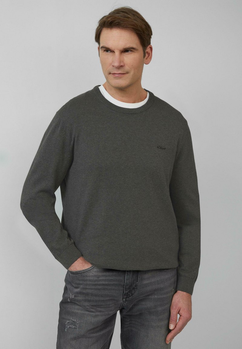 Donkergrijze sweatshirt met een ronde hals en lange mouwen. Bevat een subtiele logo op de borst. Draagt over een witte crew neck shirt en gecombineerd met grijze jeans.