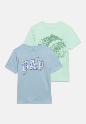 Deux t-shirts à manches courtes : bleu clair avec "GAP" et petits motifs de poissons, vert menthe avec une illustration de montagne et de vague.