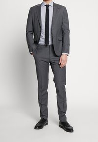 Gray suit with a slim fit, featuring a notch lapel and two-button closure. Paired with a striped shirt and black tie, complemented by black shoes.