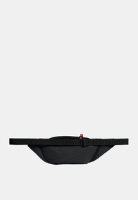 Sort stof bæltepose med struktureret finish, lynlåslomme og justerbar rem. Udstyret med et lille schweizisk flag som accent.