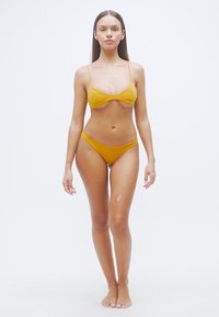 Ensemble bikini jaune moutarde au design minimaliste. Le haut comporte de fines bretelles et un devant légèrement torsadé, tandis que le bas est coupé taille basse.