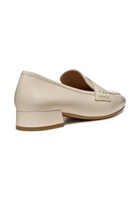 Mocassino in pelle beige con tacco basso a blocco, punta arrotondata e dettagli decorativi cuciti sul davanti. Texture liscia e design minimal.