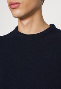 Suéter de punto color azul marino con cuello redondo, que presenta una tela texturizada y un sutil ribete en el cuello para un detalle adicional.