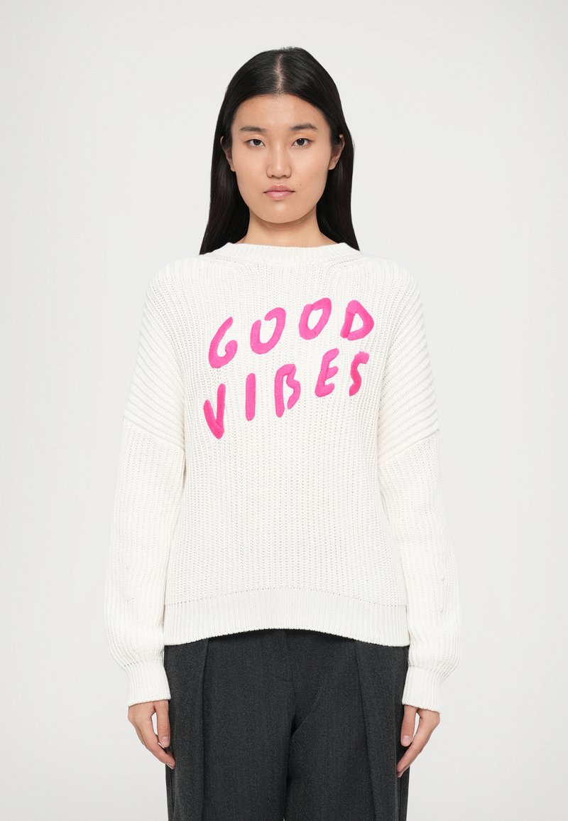 Biely pletený sveter s rebrovanou textúrou, s výrazným ružovým nápisom "GOOD VIBES". Voľný strih a spadnuté ramená.