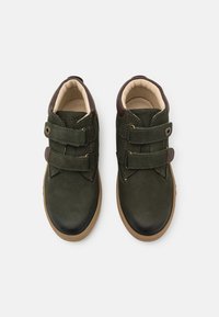 Zapatos de cuero verdes con dobles correas de Velcro, acentos marrones y un interior beige; punta redondeada y suela texturizada.