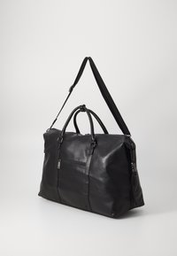 Black leather duffle bag with a textured finish, dual top handles, adjustable shoulder strap, and a front zip pocket.