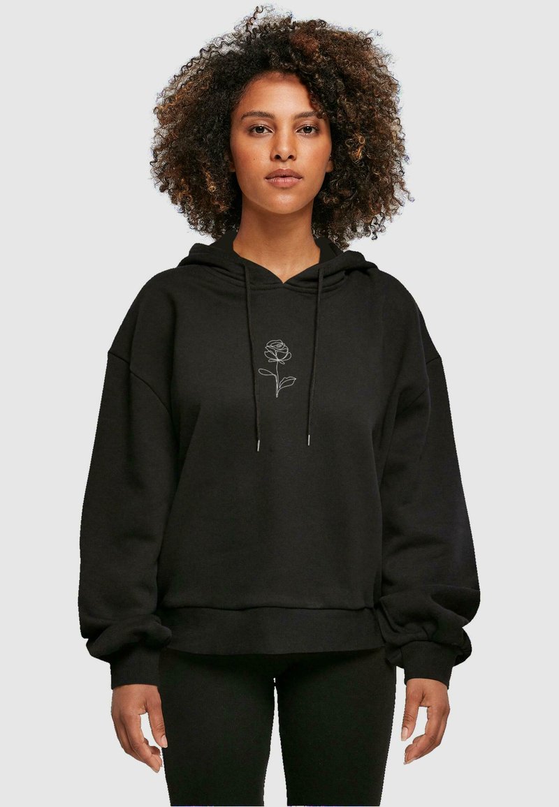 Sudadera negra de material suave con un corte relajado, que presenta un bordado de rosa blanca en el centro y capucha con cordón. Mangas largas.