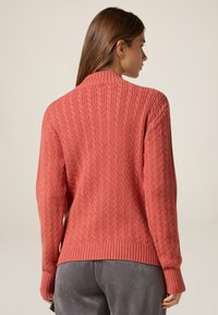 Suéter de lana color rosa con un diseño de punto en relieve, cuello alto y dobladillos y puños acanalados. Vista posterior que resalta los detalles de la costura.