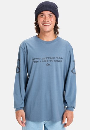 Blauwe longsleeve shirt met een grafische slogan in donkergrijs, met een ontspannen pasvorm en geribbelde manchetten. Casual denim broek en een marineblauwe beanie.