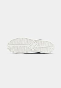 Semelle de sneaker blanche avec une texture en caoutchouc antidérapant. Présente un bord lisse et un logo central de couleur contrastante. Design minimaliste.