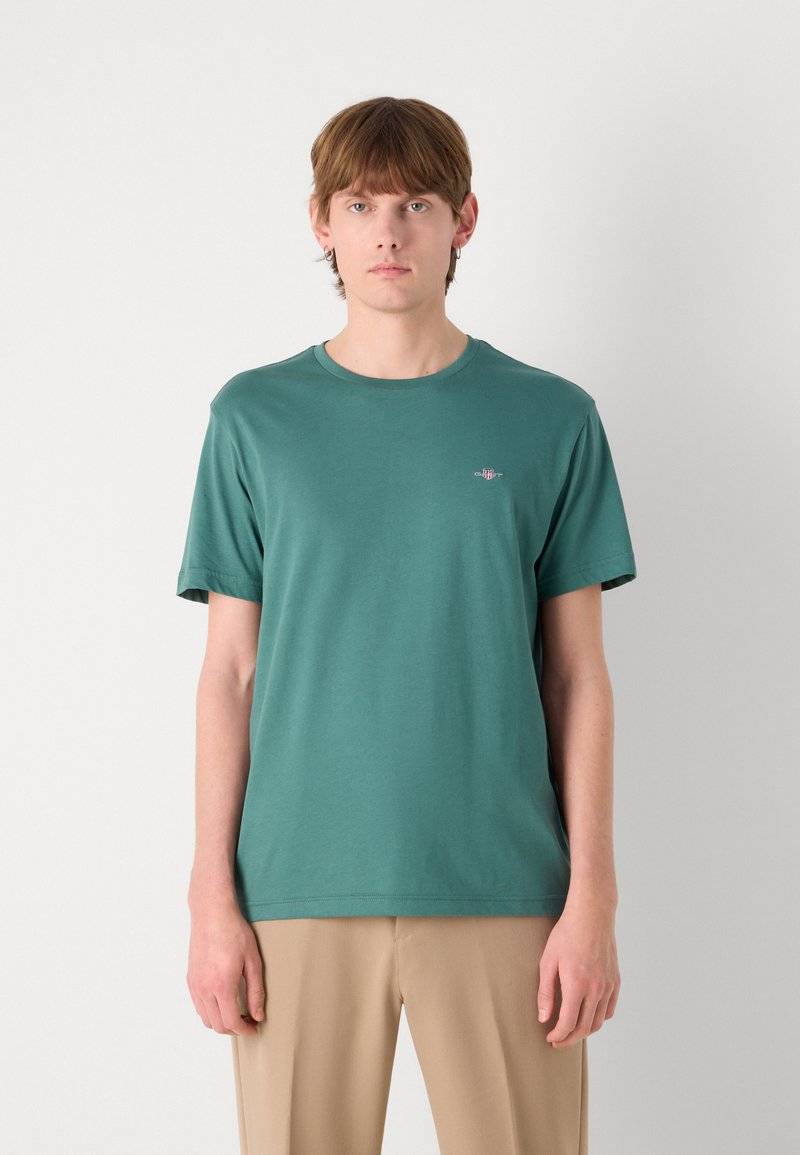 Bequem geschnittenes grünes Baumwoll-T-Shirt mit Rundhalsausschnitt, kurzen Ärmeln und einem kleinen gestickten Logo auf der Brust. Glatte Textur.