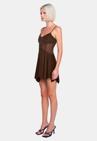 Braunes ärmelloses Kleid mit durchsichtigen Einsätzen, ausgestellt gesäumt und mit taillierter Passform. Kombiniert mit schwarzen Riemchen-Heels. Glatte Stofftextur.