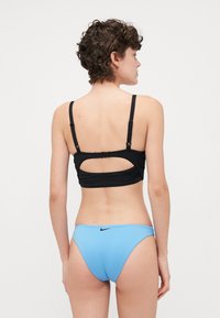 Čierny bikini top s nastaviteľnými popruhmi a vyrezávaným chrbtom, v kombinácii s modrými bikini nohavičkami so malým logom Nike. Hladká textúra.