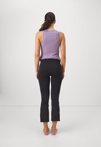 Fioletowy bezrękawnik o dopasowanym kroju, zestawiony z czarnymi spodniami sięgającymi kostek, z bocznymi rozcięciami i wysokim stanem.