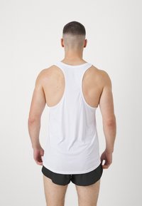 Hvid ærmeløs atletisk tanktop med rund halsudskæring, glat tekstur, og racerback-design, båret med sorte shorts.