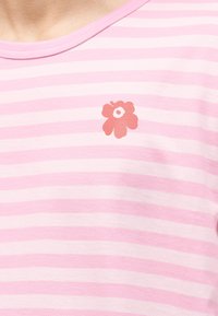 Rožnato in belo obarvano tkanino z vodoravnimi črtami in majhno rdečo cvetlično grafiko blizu izreza na vratu.