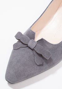 Chaussure plate en daim gris avec un bout pointu, ornée d'un nœud décoratif sur le cou-de-pied et une semelle intérieure beige lisse.