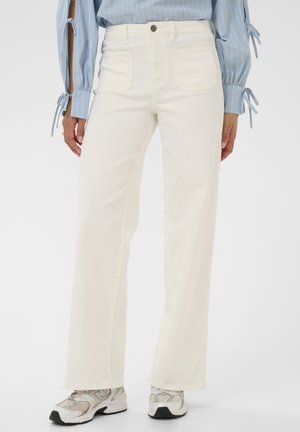 Pantalon blanc taille haute à jambes larges avec poches avant, porté avec des chaussures de sport grises et blanches, porté par une personne portant une chemise à rayures bleues.