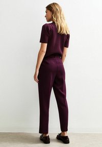 Haut à manches courtes bordeaux avec épaules froncées, associé à un pantalon ajusté assorti, texture lisse et design épuré. Des chaussures noires complètent le look.