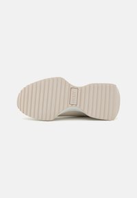 Hvit sneakersåle med et teksturert, rillet design. Har en merkbar DKNY-logo og en glatt, avrundet form.