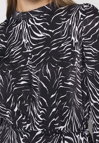 Černé šaty s výrazným bílým zebrovým vzorem, vysokým výstřihem a texturovanou látkou s detaily ve zúženém pase.