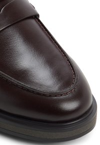 Bruin leren schoen met een gepolijste afwerking, gekenmerkt door een gestikt moccasinontwerp, een gladde textuur, een ronde neus en een contrasterende donkere zool.