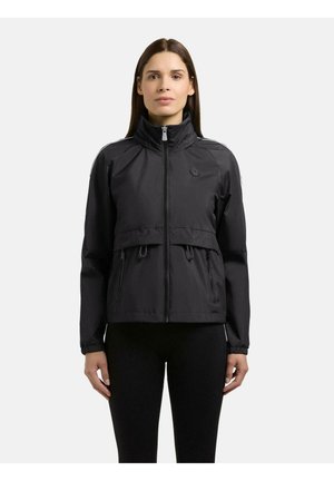 Frau mit glatten braunen Haaren, die eine schwarze Jacke mit Reißverschluss, hohem Kragen und zwei Reißverschlusstaschen trägt, steht vor einem schlichten hellen Hintergrund.