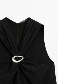 Top nero senza maniche con scollatura a V profonda, schiena plissettata e dettaglio in metallo argentato in vita. Tessuto morbido con una texture liscia.