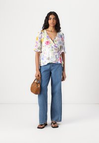 Blomsterinnpakningstopp i lett stoff med puffeerm, kombinert med høy midje denimflair. Håndholdt brun vevd veske og sorte flip-flops.