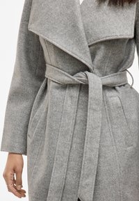 Szary płaszcz z szerokim kołnierzem, wykonany z miękkiego, teksturowanego materiału. Posiada boczne kieszenie i podkreśloną talię.