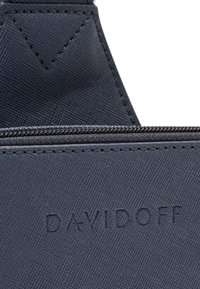 Dunkelblauer, strukturierter Stoff mit sichtbaren Nähten und geprägtem „DAVIDOFF“-Logo. Verfügt über einen Reißverschluss und ein dreieckiges Designelement.