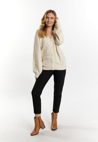 Krämfärgad cardigan med V-hals, stora knappar, strukturerad yta och pösiga ärmar. Bärs över svarta byxor och bruna klackbooties.