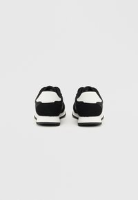 Sapatos atléticos em preto e branco com superior em camurça e malha, salto arredondado e sola de borracha texturizada, vistos de trás.