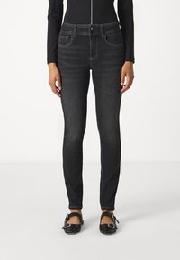 Jean skinny noir avec taille mi-haute, poches avant et détails de coutures contrastantes. Assorti à des ballerines noires à boucle.