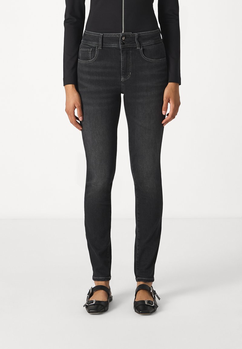 Jean skinny noir avec taille mi-haute, poches avant et détails de coutures contrastantes. Assorti à des ballerines noires à boucle.