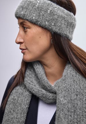 Grau gestricktes Stirnband und Schal aus flauschigem Garn, das auf dem Stirnband subtile Pailletten aufweist, vor einem neutralen Hintergrund zu sehen.