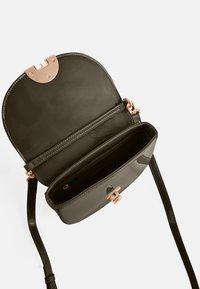 Bolso negro brillante con forma estructurada, herrajes en oro rosa, cierre de broche y una correa ajustable. El interior cuenta con un bolsillo con cremallera.