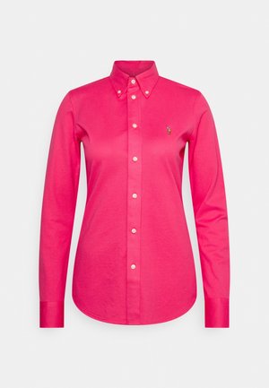Lyserød langærmet skjorte med knapper, krave og lille broderet logo på venstre bryst.