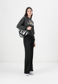 Felpa oversize nera con scritte dorate, abbinata a pantaloni neri a gamba larga e sneakers bianche. Porta una borsa nera con dettagli argentati.