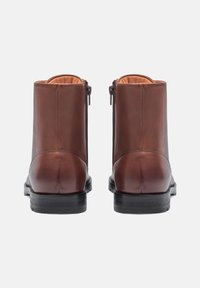 Stivali ankle in pelle marrone con una texture liscia, dotati di cerniere laterali, punta arrotondata e suola in gomma nera.