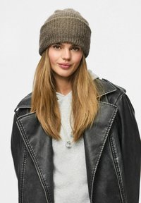 Beanie marrone a maglia con texture a coste, indossato con una felpa grigia e una giacca di pelle nera, caratterizzata da ampi reverse e una cerniera.