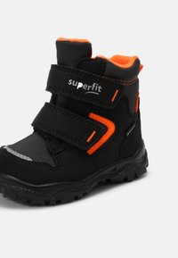 Botte d'hiver pour enfants noire et orange avec deux sangles Velcro, semelle texturée et col rembourré pour la chaleur et le soutien.
