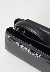Sac à main en cuir noir avec une texture lisse, comportant un logo silver "REPLAY", une poignée supérieure et une poche zippée à l'intérieur.