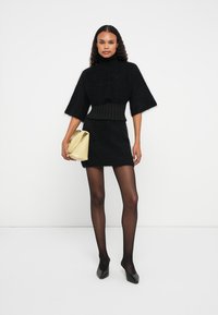 Μαύρο φuzzy πλεκτό πουλόβερ με φαρδιά μανίκια, συνδυασμένο με αντίστοιχη φούστα. Το μοντέλο κρατά μια κίτρινη τσάντα, φορά μαύρες καλσόν και ψηλές γόβες.