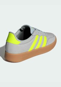 Light gray sneaker with three bright yellow stripes, textured upper, gum sole, and padded collar for comfort. adidas branding on the heel.